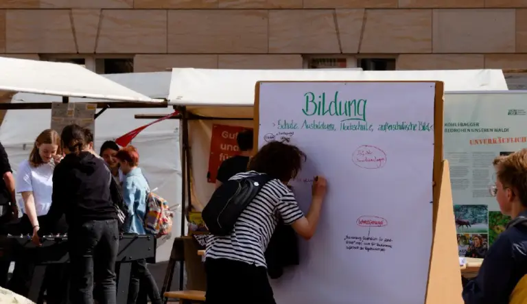 Mensch schreibt auf ein Flipchart unter dem Titel "Bildung" auf einem Markt.